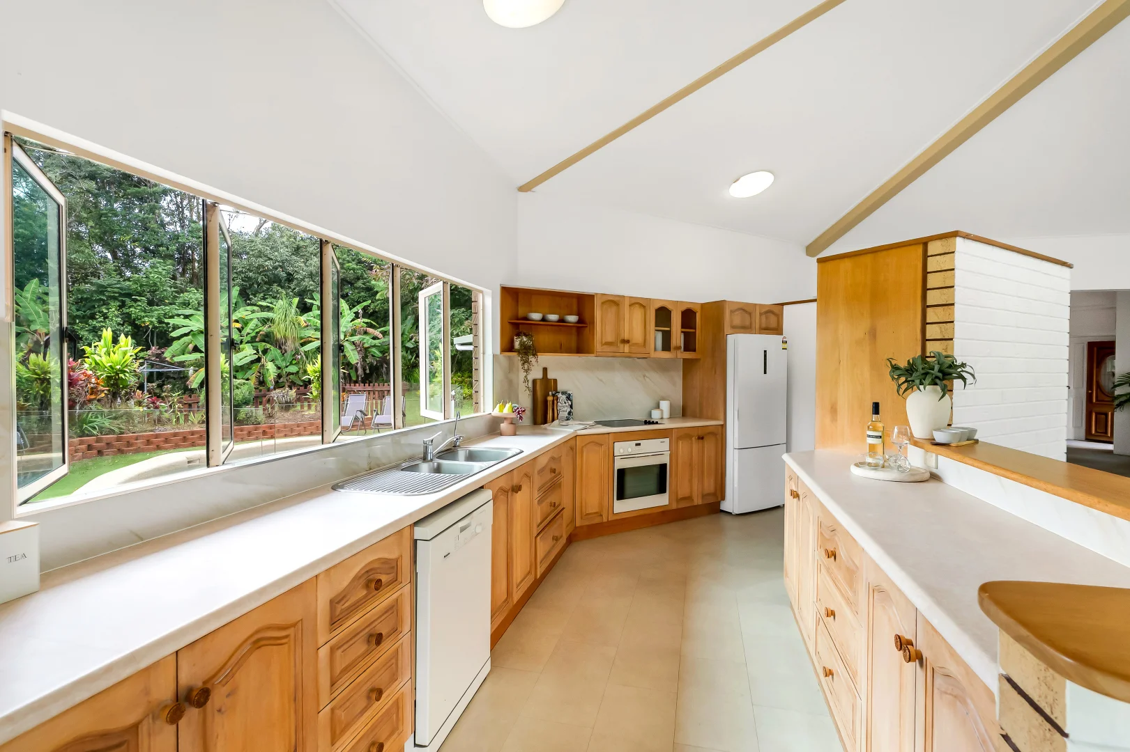 Timber kitchen with wide windows opening to tropical greenery